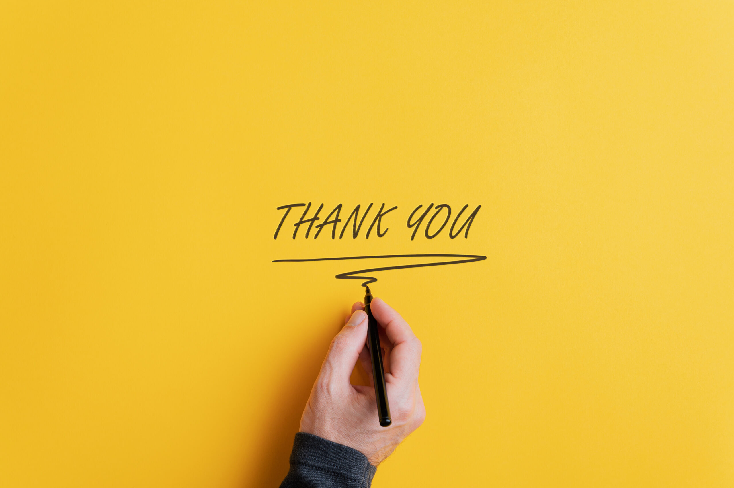 Male hand writing a Thank you sign with black marker on a yellow background. With copy space ready for your text.